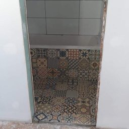 Ben-Bud - Fragment łazienki w trakcie prac: dekoracyjne płytki podłogowe w stylu patchwork układane na klej, widoczne białe płytki na ścianie, surowy stan wykończenia przy progu.