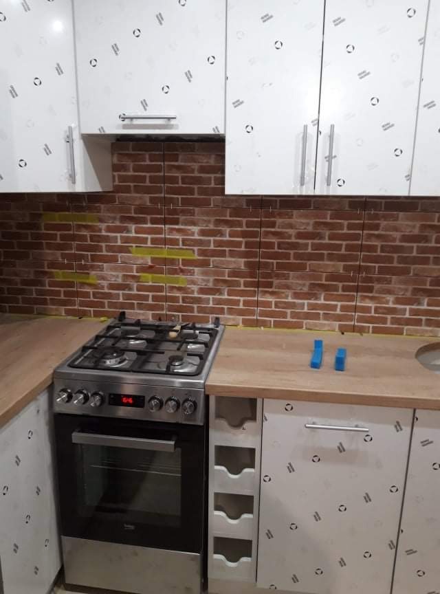 Kuchnia po częściowym ułożeniu cegieł na ścianie, widoczne żółte ślady po kleju, białe szafki z delikatnym wzorem, kuchenka gazowa z piekarnikiem.