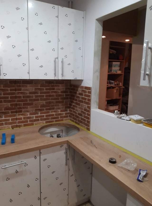 Montaż ceglanej ściany nad blatem kuchennym z wyciętym otworem na zlew, szafki górne w folii ochronnej, widoczne narzędzia i materiały na blacie.