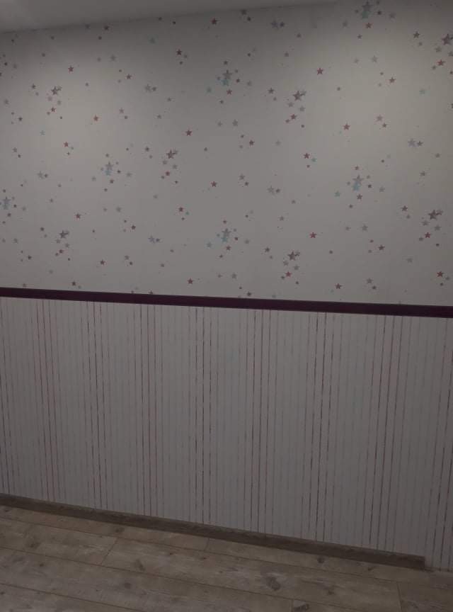 Pokój dziecięcy po odświeżeniu: Białe ściany z motywem gwiazd (czerwone i niebieskie), dolna część ściany wykończona panelami ściennymi w pionowe paski, podłoga z paneli drewnopodobnych.