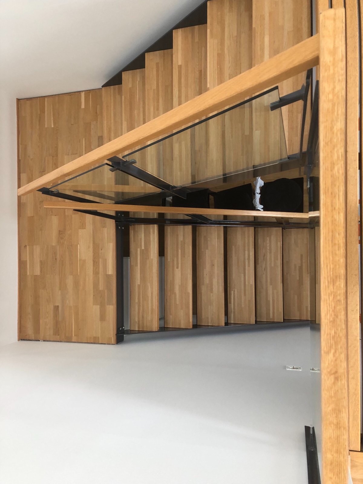 Drewniane schody z metalową konstrukcją i szklanymi barierkami, widok z góry, jasne wnętrze.