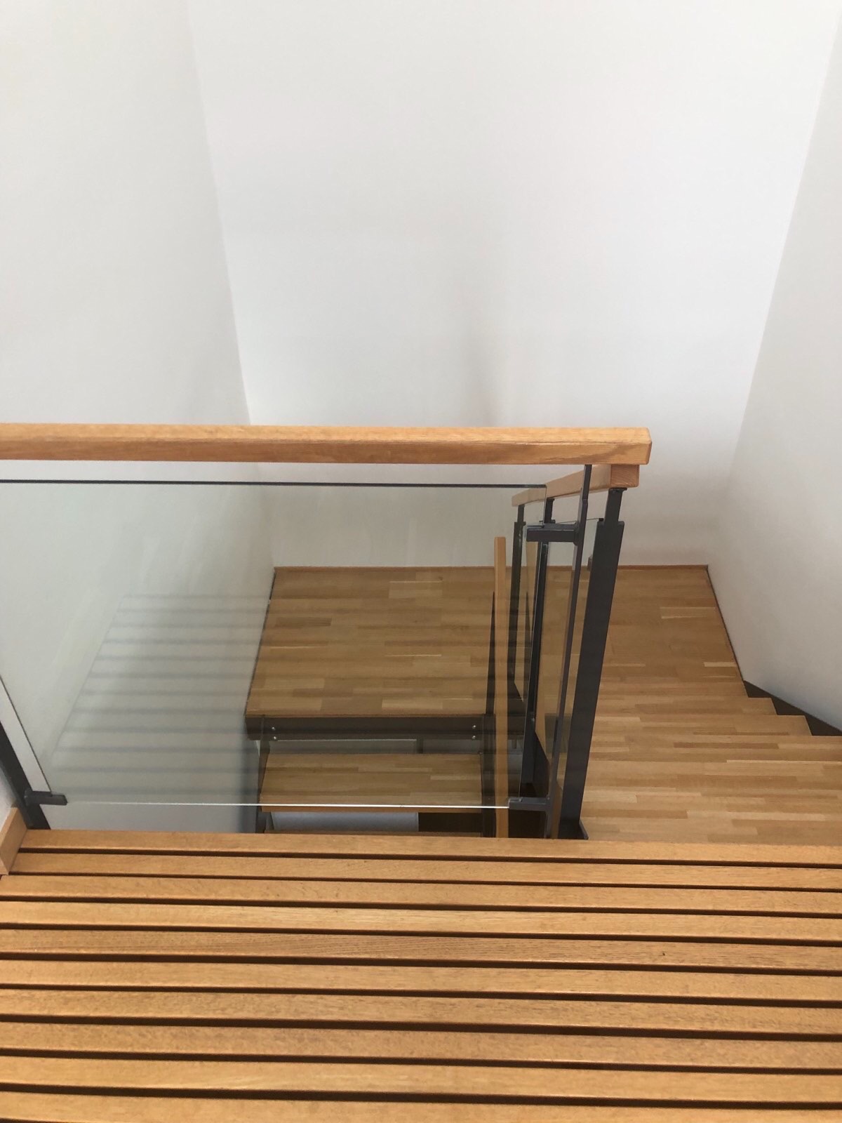 Nowoczesne schody drewniane z przeszkloną balustradą i metalowymi elementami, widok z góry na stopnie z wyraźnym usłojeniem drewna.