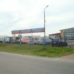 Plac z samochodami używanymi z banerami reklamowymi Auto Handel Cars-Du-Mar w pochmurny dzień.