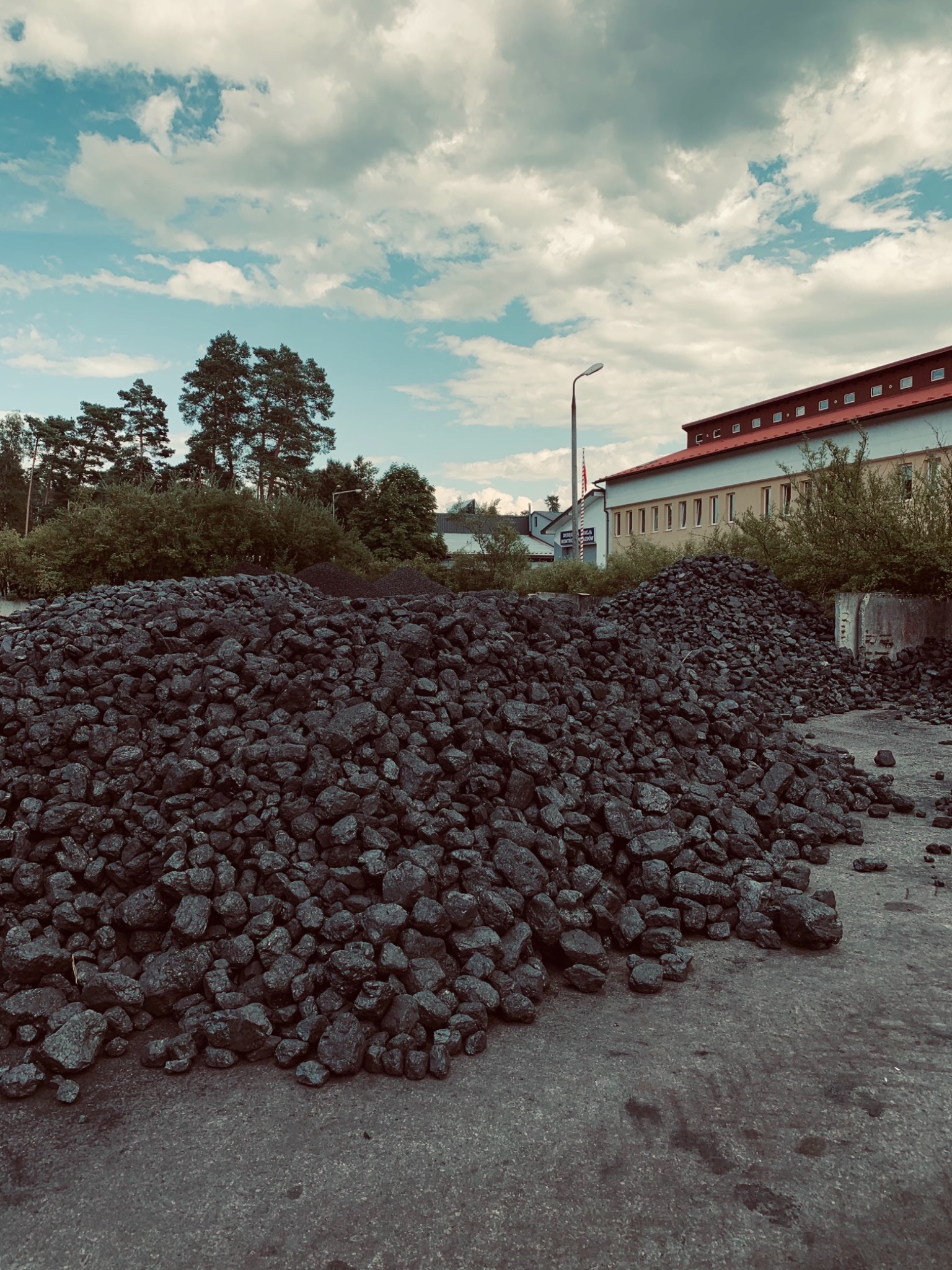 Góra czarnego węgla kamiennego na placu składowym, budynek w tle pod błękitnym niebem z chmurami.