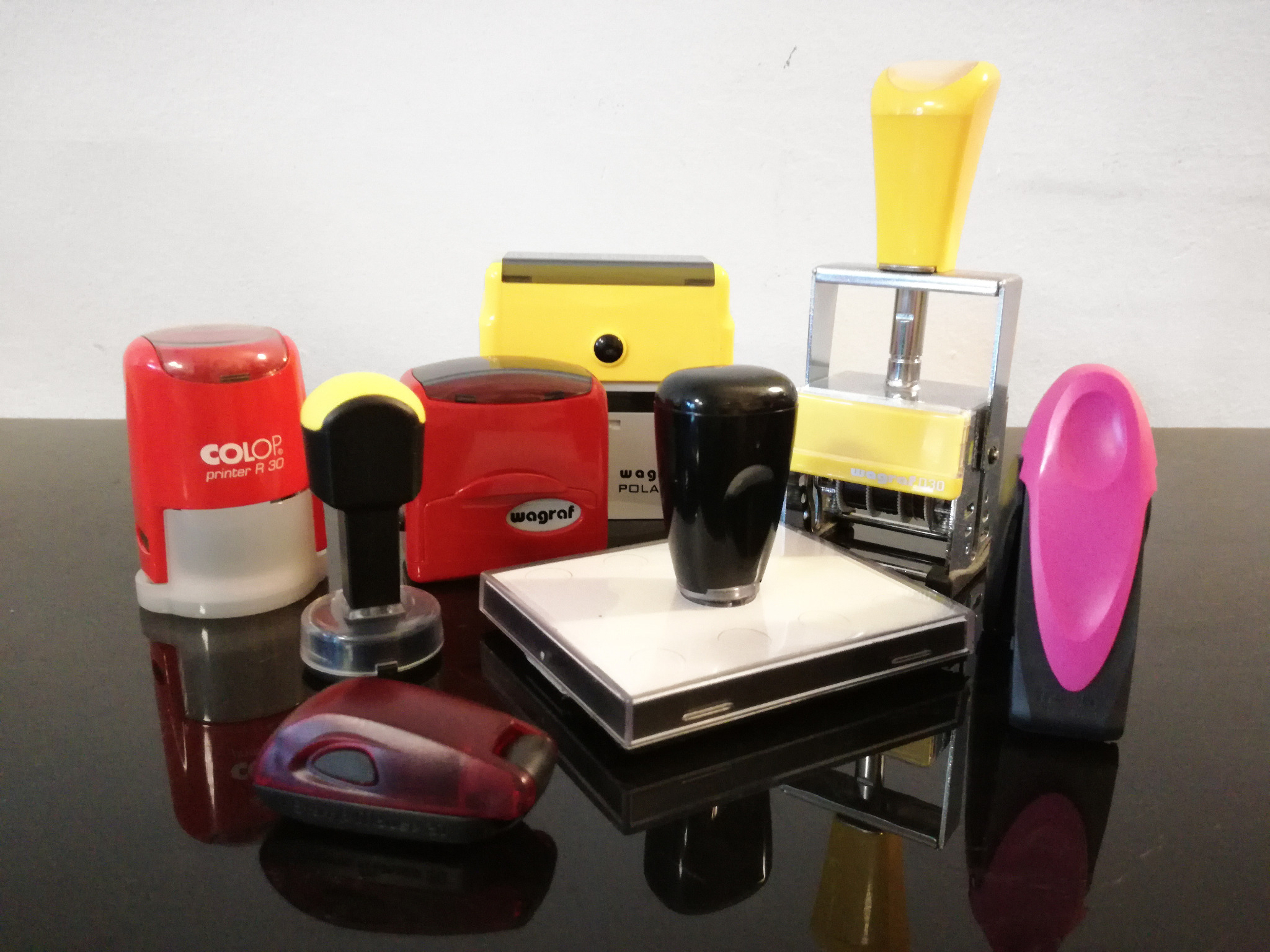 Różnokolorowe automatyczne pieczątki biurowe w zbliżeniu, widoczne marki Colop, Wagraf i Polan