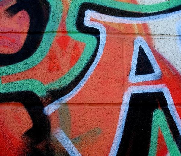 Fragment ściany z betonu komórkowego pokrytej wielobarwnym graffiti w odcieniach czerwieni, zieleni i czerni, z wyraźnymi konturami w kolorze białym.