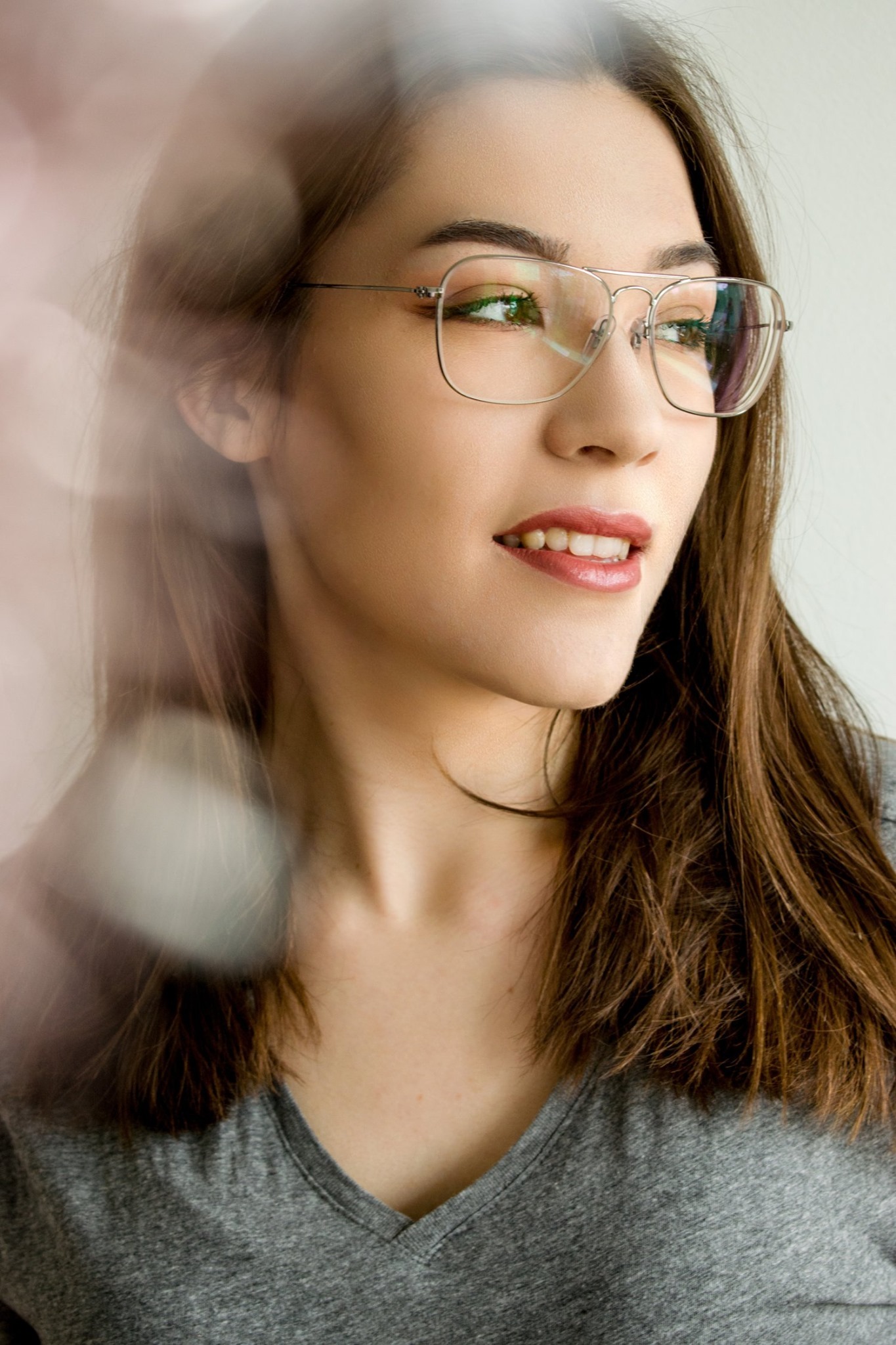 Portret kobiety w okularach z metalowymi oprawkami, patrzącej w bok, z efektem bokeh na pierwszym planie.