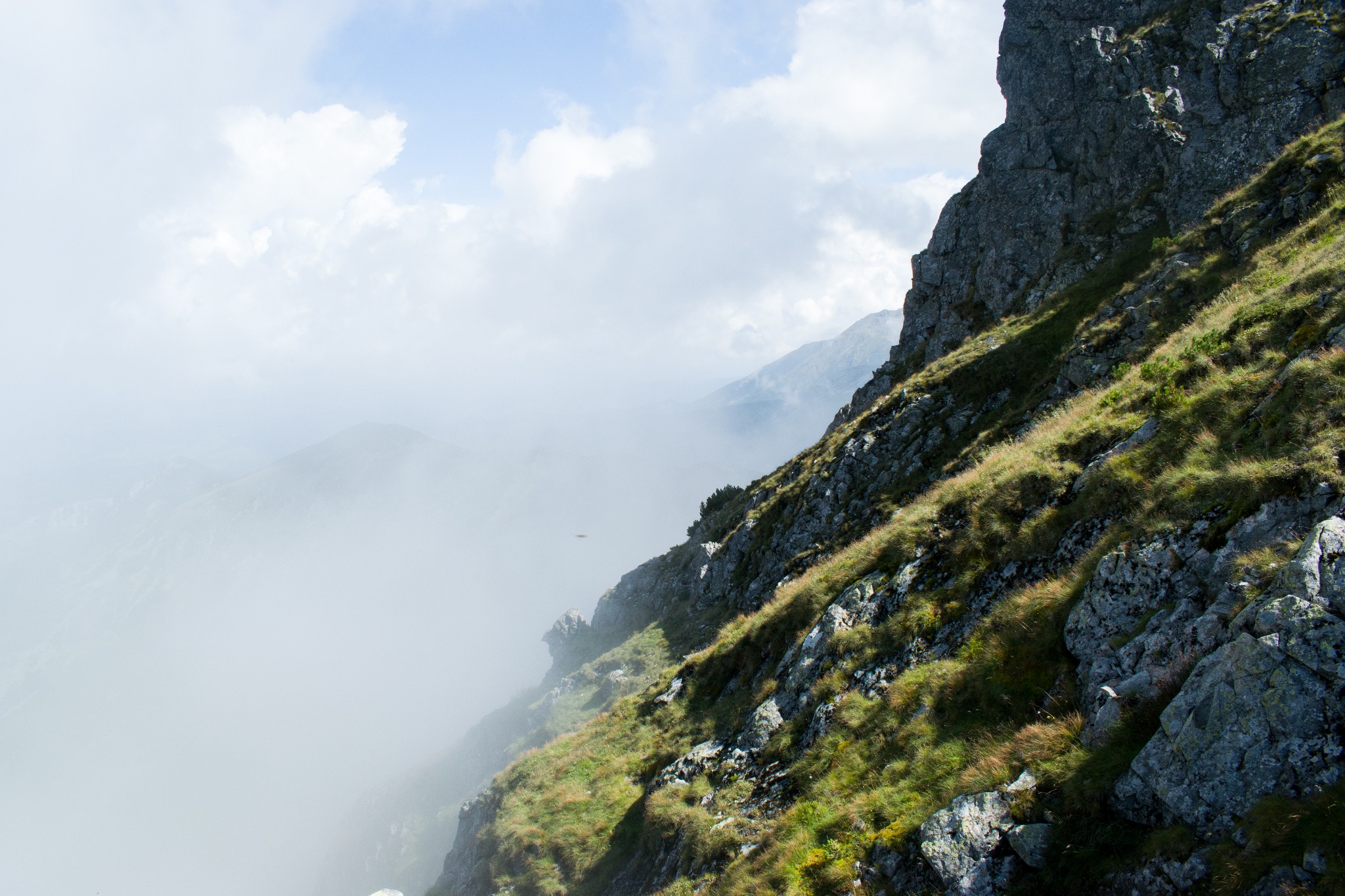Skała porośnięta trawą na tle gór spowitych mgłą, widok z góry w pochmurny dzień.