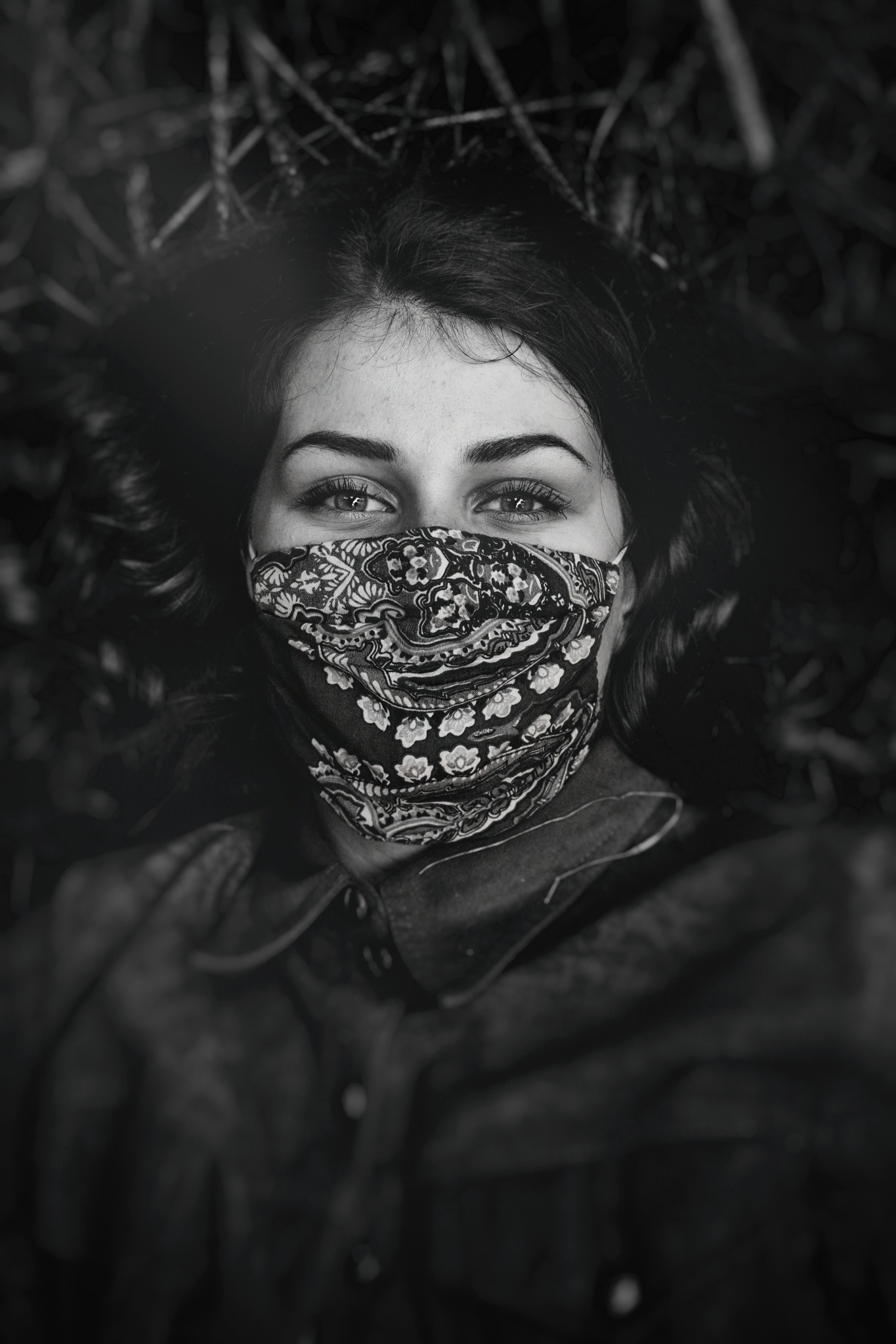 Portret kobiety z wzorzystą maską na twarzy, leżącej na trawie, w czerni i bieli.