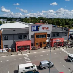 Szeroki kadr z lotu ptaka na budynek składu materiałów budowlanych Grupa PSB FIMAL z zaparkowanymi samochodami dostawczymi i ułożonymi paletami z towarem na zewnątrz.