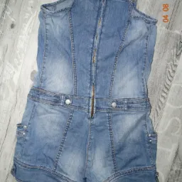 Używany dżinsowy kombinezon damski z rozpiętym zamkiem błyskawicznym na plecach, leżący na podłodze z paneli.