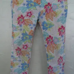 Spodnie damskie z kolorowym, kwiatowym wzorem na białym tle, widoczne zapięcie na guzik.