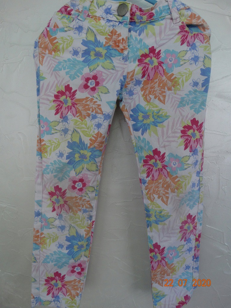 Spodnie damskie z kolorowym, kwiatowym wzorem na białym tle, widoczne zapięcie na guzik.