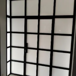 Czarna, metalowa konstrukcja drzwi z mlecznymi szybami, widoczny zamek i kluczyk.