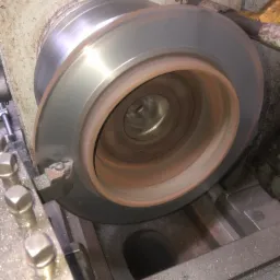 Metalowy element obrabiany na tokarce, widoczne wióry i narzędzie skrawające.