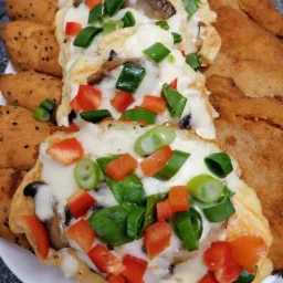 Bliny z pieczarkami i serem, udekorowane czerwoną papryką i szczypiorkiem, obok kotlety panierowane i krokiety z czarnuszką na białym talerzu.