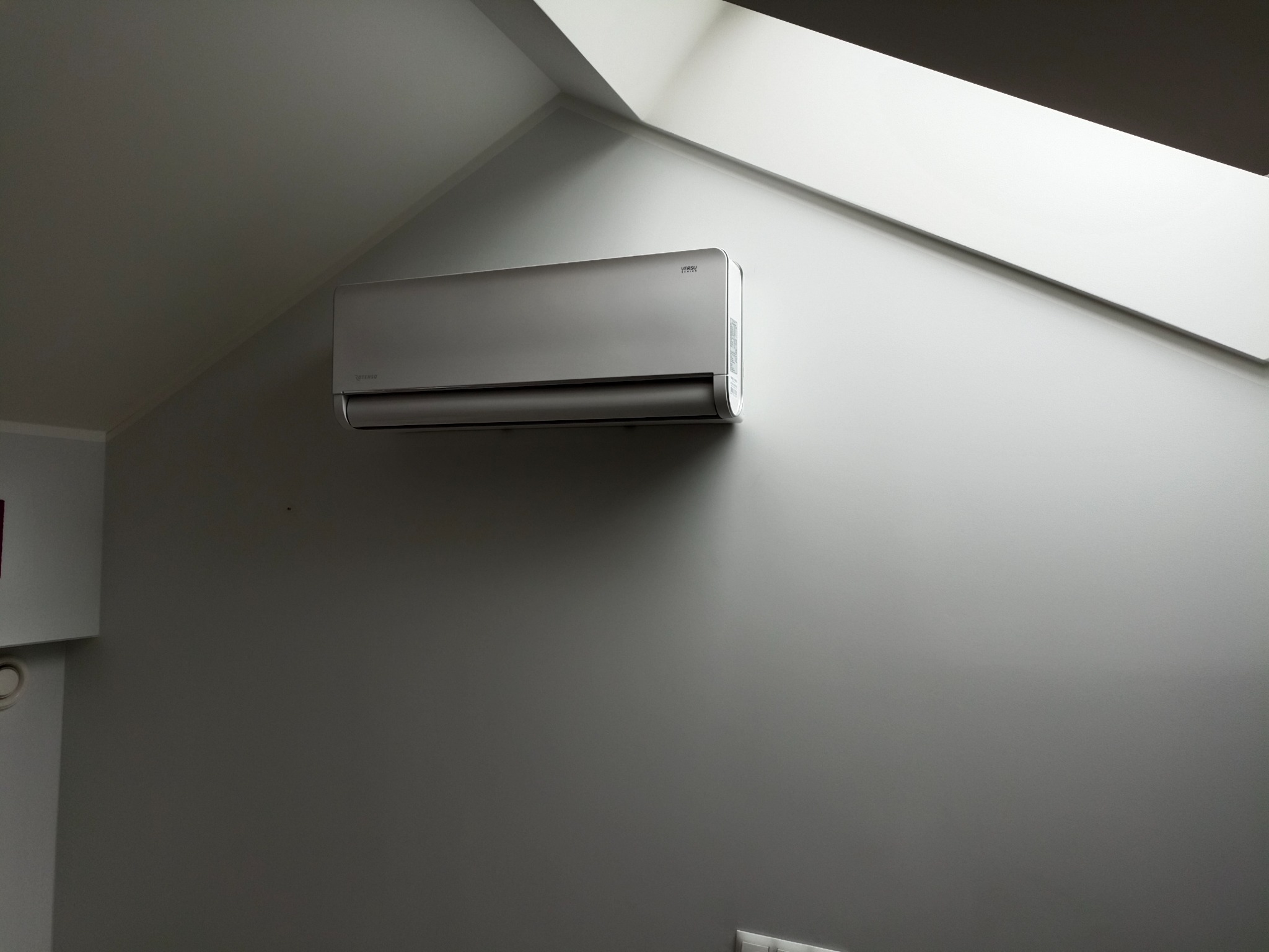 Zamontowany srebrny klimatyzator marki Versu w szarym pomieszczeniu na poddaszu z oknem dachowym, Jaworze.