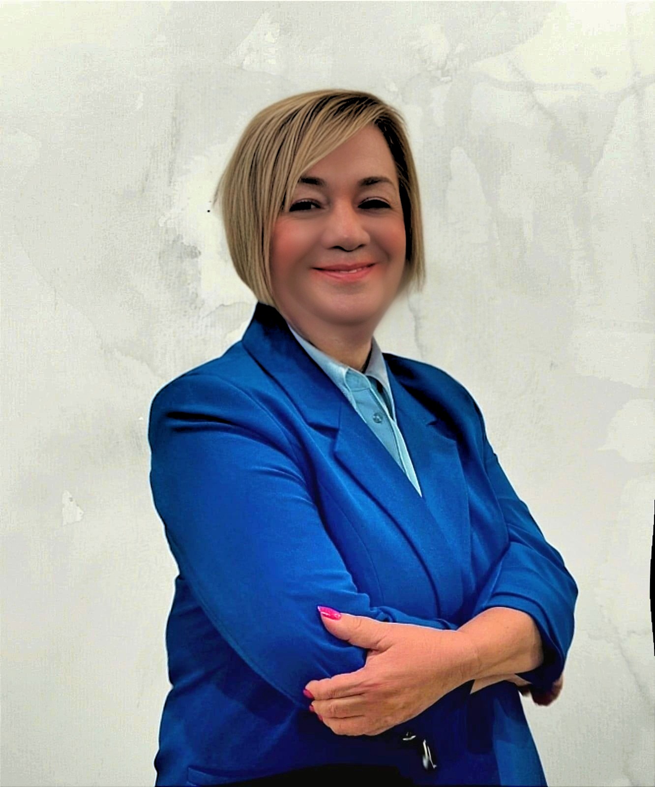 Portret uśmiechniętej kobiety w niebieskim garniturze na tle teksturowanej ściany, z rękami skrzyżowanymi na piersiach.
