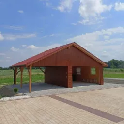 Nowoczesna, brązowa konstrukcja z drewna z czerwoną dachówką, pełniącą funkcję garażu i zadaszonego miejsca postojowego, z otwartym bokiem i drzwiami, na wybrukowanym podjeździe z widokiem...