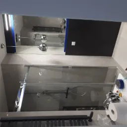 Nowoczesna kabina prysznicowa z szklanymi drzwiami i chromowaną armaturą, widok z perspektywy montażu, z widocznymi materiałami zabezpieczającymi i taśmą malarską.