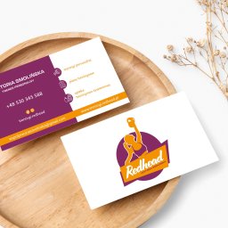 Business Partners Club - Dwie wizytówki na drewnianej tacy z suszonymi kwiatami. Jedna wizytówka w kolorze fioletowym i złotym zawiera dane kontaktowe trenera personalnego, druga wizytówka z logo firmy treningowej...