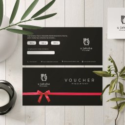 Business Partners Club - Dwa czarne vouchery prezentowe restauracji 'U Jakuba' z czerwonymi wstążkami, biała wizytówka z logo, ceramiczny wazon i świecznik na tle drewnianych desek.