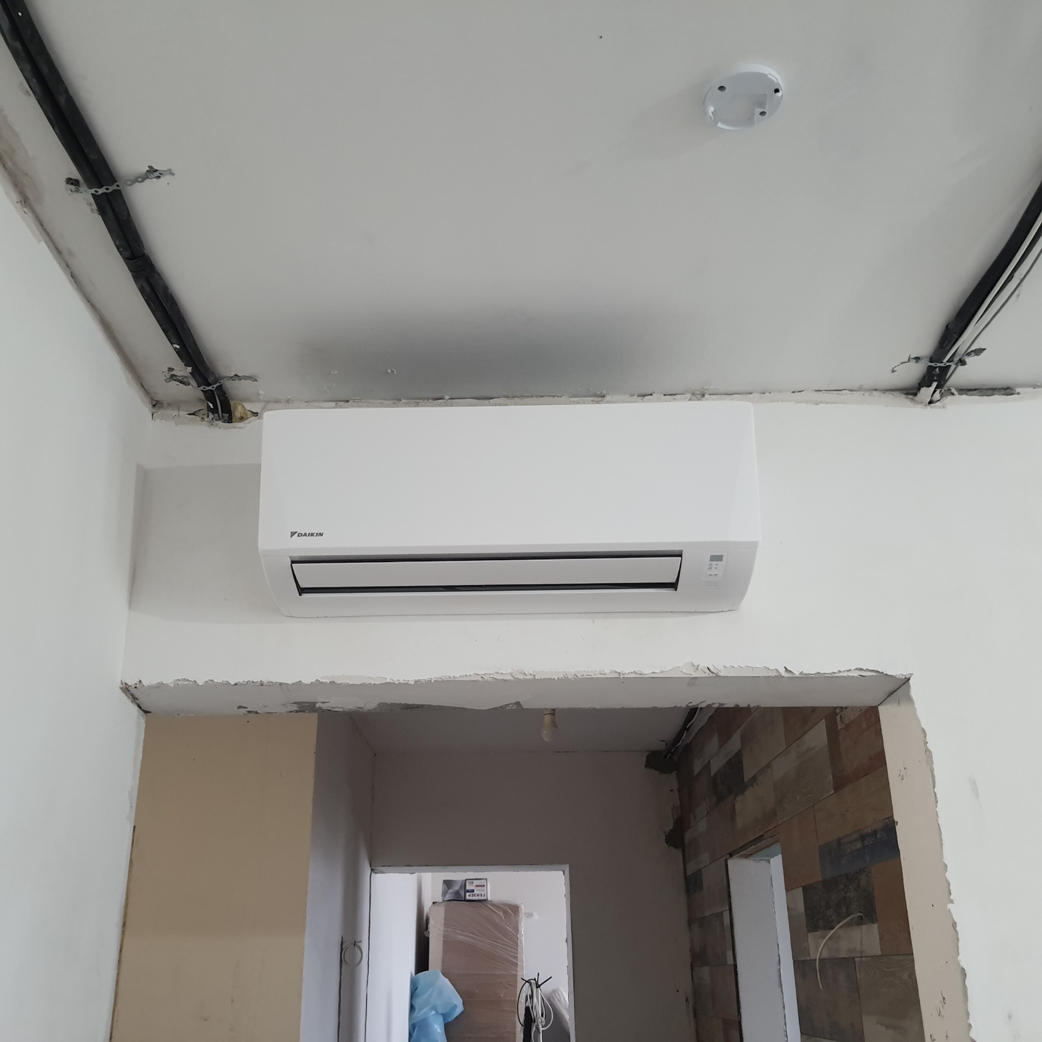 Biały klimatyzator Daikin zamontowany na ścianie w trakcie remontu, widoczne przewody i niedokończone wykończenie sufitu.