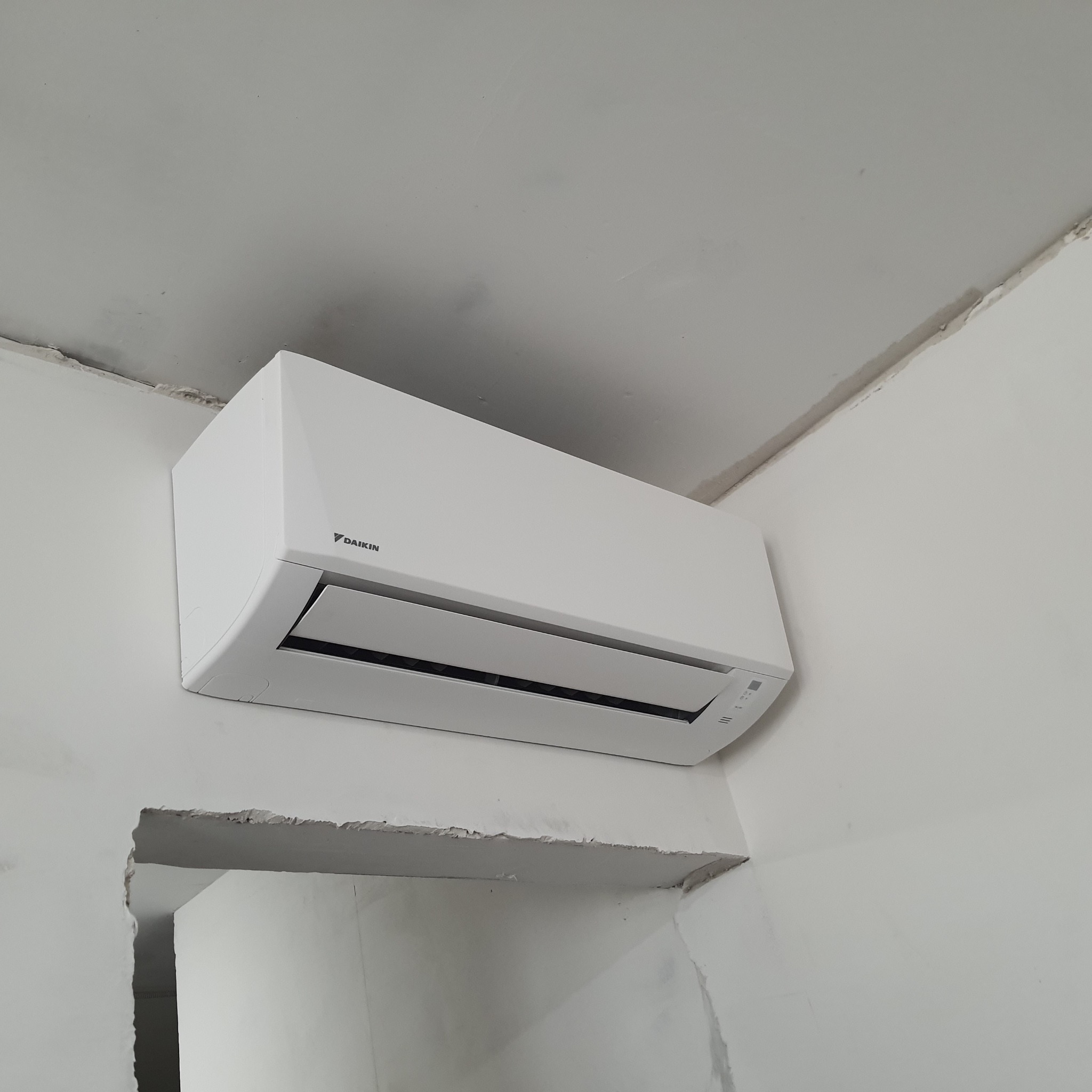 Biała jednostka wewnętrzna klimatyzacji Daikin zamontowana na ścianie w trakcie remontu, widoczne niedokończone krawędzie otworu w ścianie.