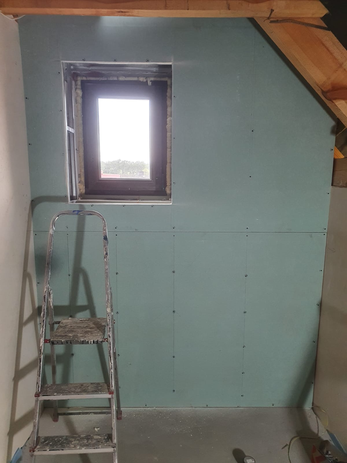 Montaż płyty karton gips w Kamsdorf na poddaszu, widoczne okno dachowe z pianką montażową i drabina.