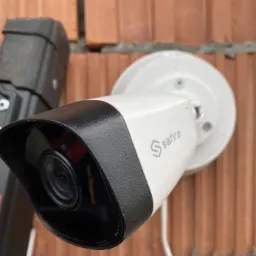 Kamera Safire zamontowana na ceglanej ścianie, obok drabiny z pomarańczowym kółkiem, widoczne ślady montażu.