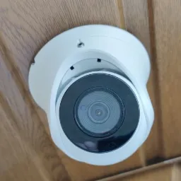 Kamera kopułkowa w obudowie z tworzywa, zamontowana na drewnianym suficie z boazerii, widok od dołu.