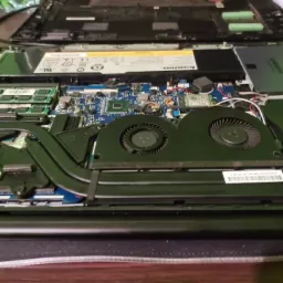 Otwarty laptop Lenovo z widocznymi komponentami wewnętrznymi: dwa wentylatory, płyta główna, pamięć RAM, dysk SSD Samsung, bateria. Górna obudowa laptopa odłożona na bok, ukazująca jej wewnętrzną...