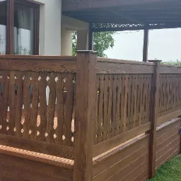 Zadaszony taras z drewnianą balustradą o dekoracyjnym wzorze, schody wejściowe na taras, widok na ogród.