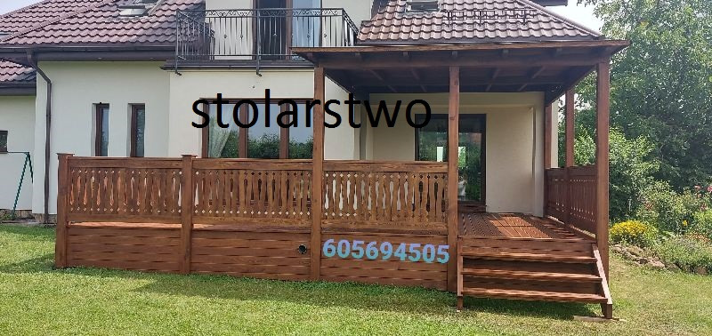 Drewniany taras z ażurową balustradą i zadaszeniem przy domu jednorodzinnym, widok z poziomu trawnika.