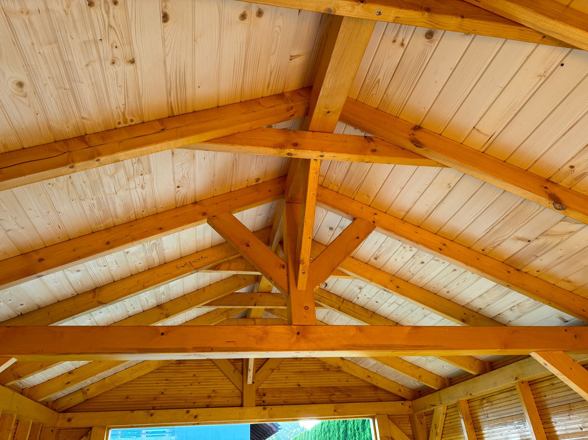 Wnętrze drewnianej konstrukcji z widocznym dachem z desek i drewnianymi belkami nośnymi, jasne drewno, częściowo zaimpregnowane, widok z dołu.