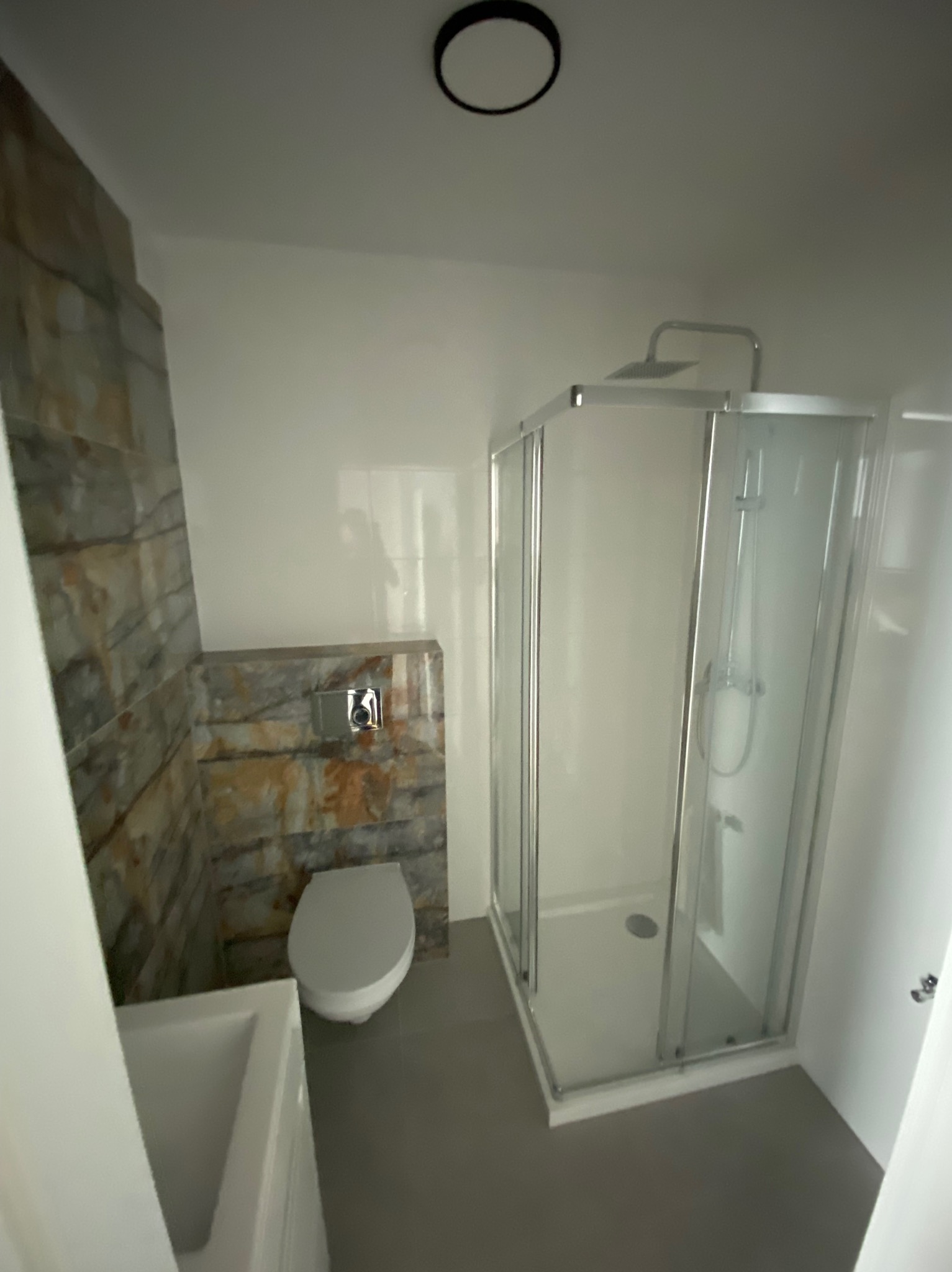 Nowoczesna łazienka z kabiną prysznicową, toaletą podwieszaną i umywalką, wykończona płytkami imitującymi kamień.