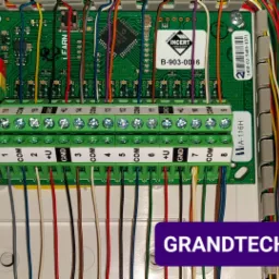 Panel sterowania systemu alarmowego z podłączonymi kolorowymi przewodami, widoczne złącza śrubowe i oznaczenia pinów, etykieta 'INCERT CERTIFICATION'.