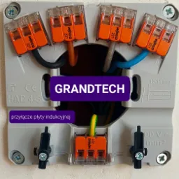 Podłączenie przewodów do kostki WAGO 221 w puszce elektrycznej, widoczne przewody w kolorach czarnym, brązowym, szarym, niebieskim i żółto-zielonym, przyłącze płyty indukcyjnej.