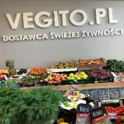 Stoisko z różnorodnymi świeżymi owocami i warzywami, w tle logo 'VEGITO.PL - DOSTAWCA ŚWIEŻEJ ŻYWNOŚCI' na szarej ścianie.