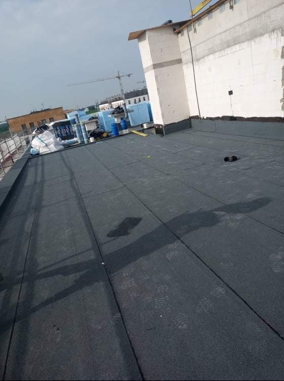 Wykończony dach pokryty papą termozgrzewalną we Wrocławiu, widok z góry, na dachu widoczne materiały budowlane i narzędzia.