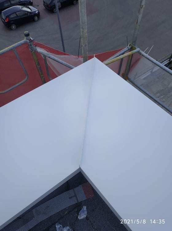 Widok z góry na fragment dachu z obróbką blacharską w kolorze białym, widoczne rusztowanie i fragment ulicy z samochodami w tle.