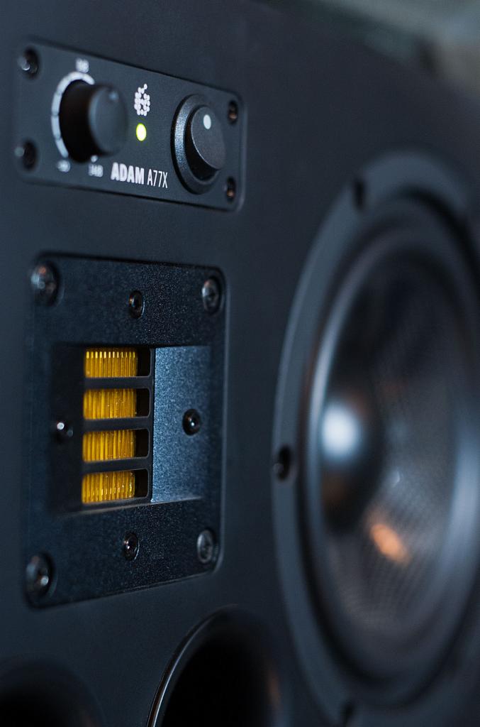 Bliski kadr monitora studyjnego ADAM A77X z widocznymi regulatorami, głośnikiem wysokotonowym i fragmentem niskotonowego, podkreślający detale sprzętu audio.