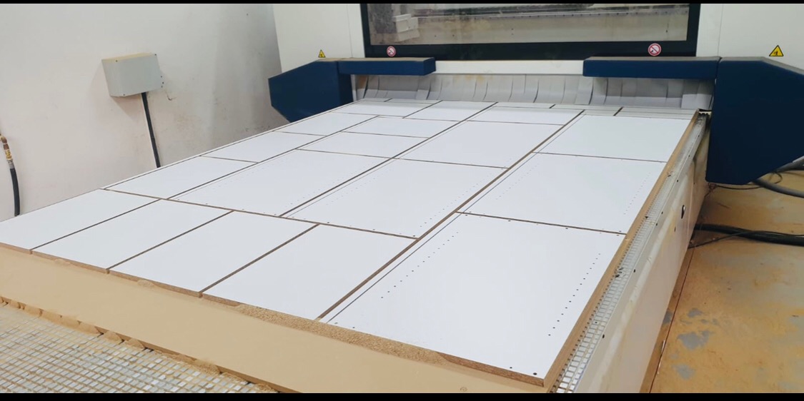 Frezarka CNC obrabia białe panele meblowe na płycie MDF, widoczne nawiercone otwory.
