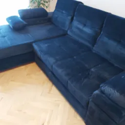 Narożnik tapicerowany w odcieniach granatu, z poduszkami, na parkiecie, w tle roślina doniczkowa.