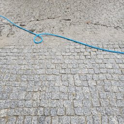 Wysokociśnieniowi Marcin Szczepanik - Szara kostka brukowa częściowo umyta, z widocznym niebieskim wężem ogrodowym.