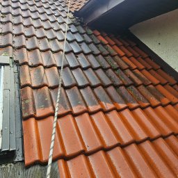 Wysokociśnieniowi Marcin Szczepanik - Częściowo wyczyszczony dach z czerwonej dachówki, widoczna lina zabezpieczająca. Połowa dachu pokryta mchem, druga połowa czysta i mokra po umyciu.