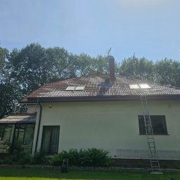 Wysokociśnieniowi Marcin Szczepanik - Dom z jasną elewacją i częściowo umytym, brudnym dachem. Przystawiona drabina, widoczne ślady po czyszczeniu. Tło: zieleń drzew i błękitne niebo.