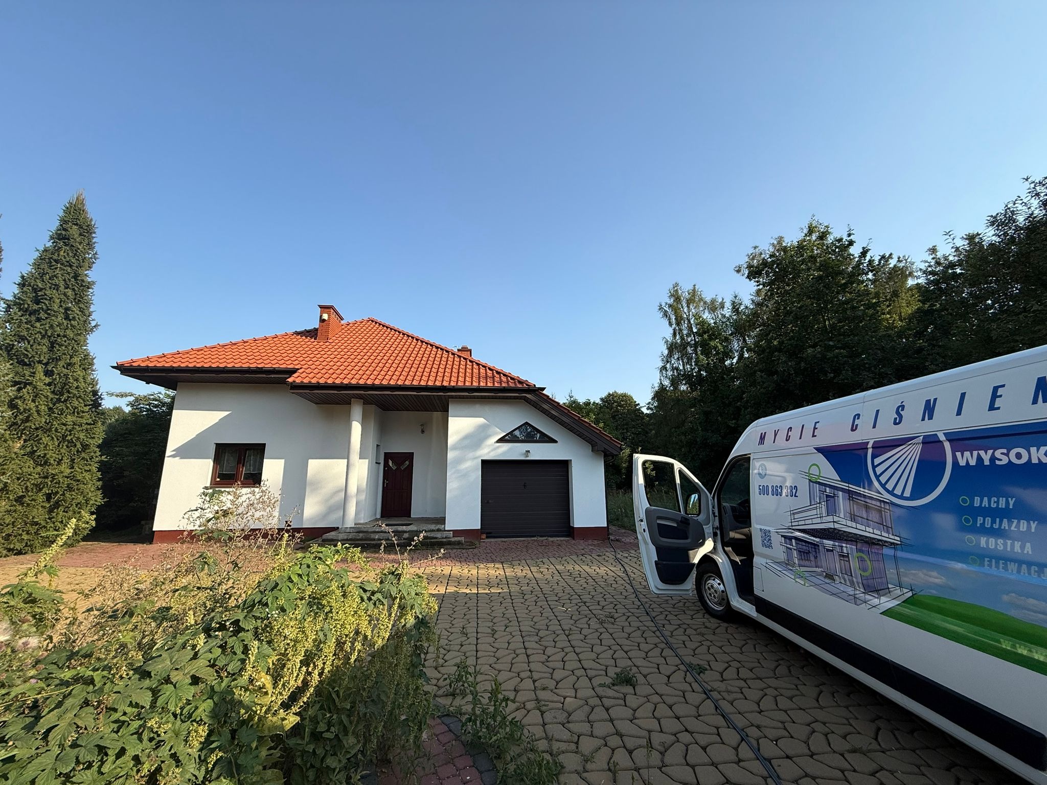 Dom jednorodzinny przed myciem elewacji, widoczny samochód firmy czyszczącej w Krosna-Parcela z reklamą mycia ciśnieniowego dachów, elewacji i kostki.