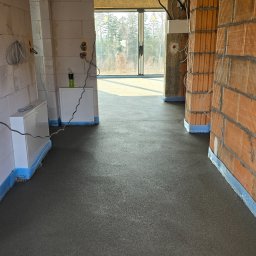 Świeża, gładka wylewka w surowym wnętrzu budynku w Stronie Śląskie. Widoczne ściany z pustaków i instalacje elektryczne. Ochrona przeciwwilgociowa przy ścianach.