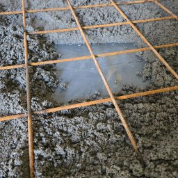 Wylewka jastrychowa zbrojona siatką stalową, częściowo pokryta folią. Widoczne nierównomierne rozprowadzenie masy jastrychowej. Detal z budowy posadzki.